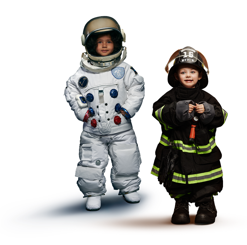 Due bambini in costume: uno indossa una tuta da astronauta con casco, l’altro una divisa da pompiere con casco e torcia.